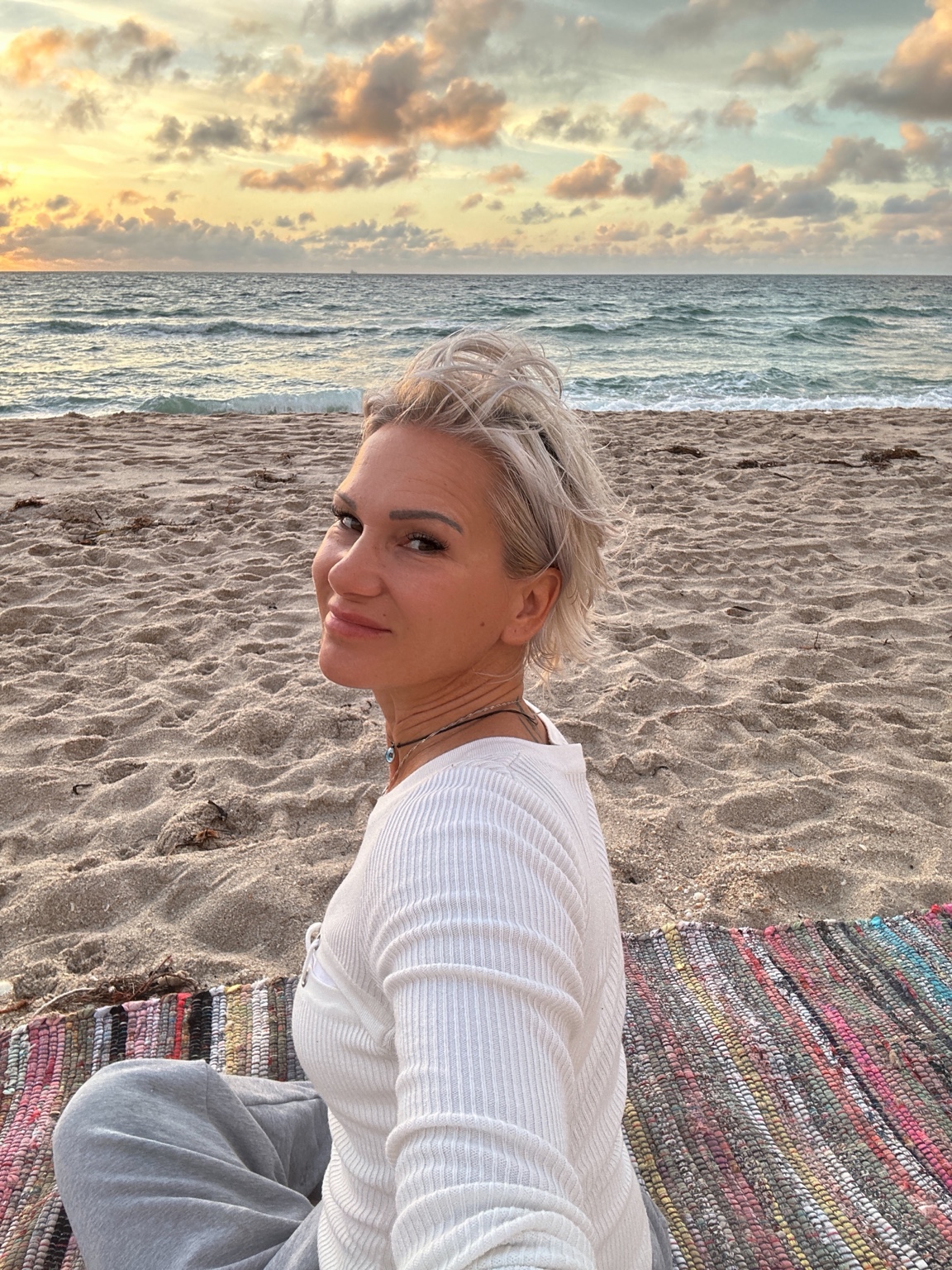 Gabriella sitting on the beach beside the ocean at sunrise